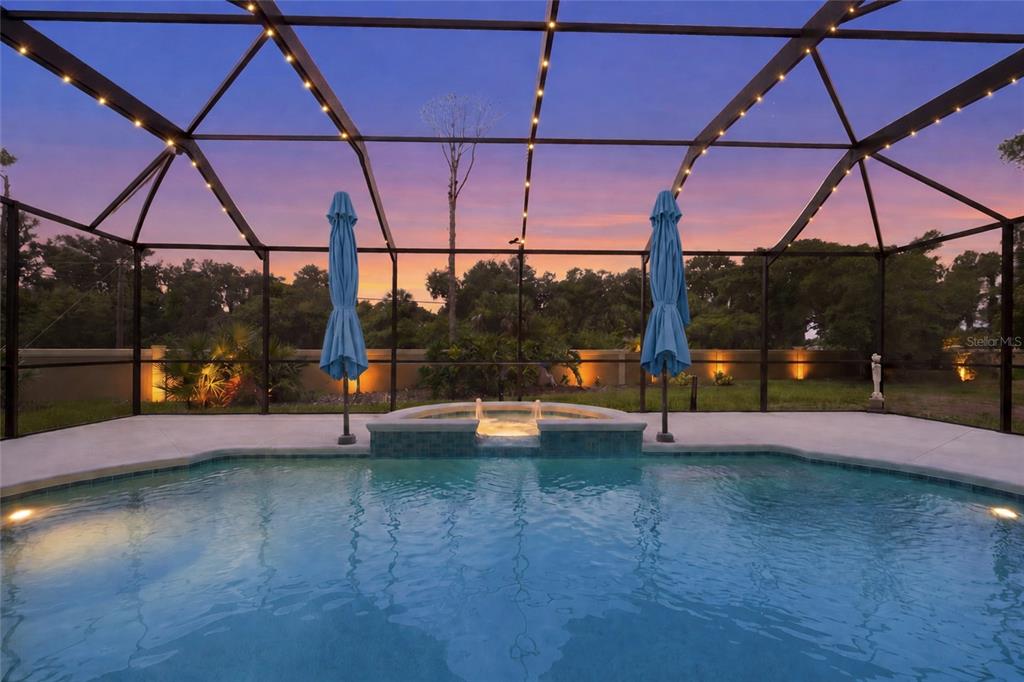 A swimming pool with an attached spa sits inside a screened-in patio at sunset — 6312 TURNERS GAP ROAD, BRADENTON, FL