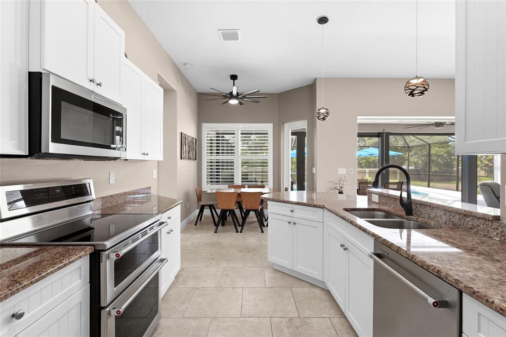 A kitchen with white cabinets, granite countertops, stainless steel appliances, and an adjacent dining area — 6312 TURNERS GAP ROAD, BRADENTON, FL