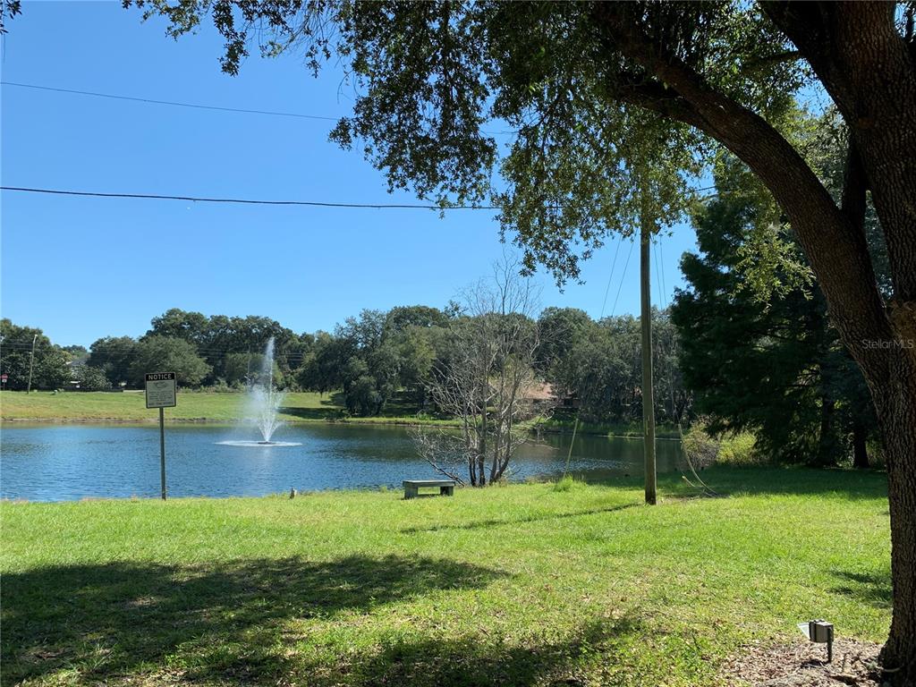 A grassy lawn overlooks a pond with a fountain and surrounding trees under a clear sky — 3550 N LAKESIDE VILLAGE DRIVE, BEVERLY HILLS, FL