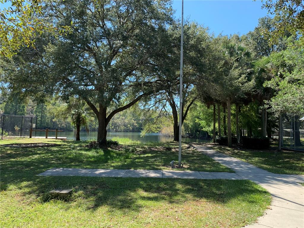 A paved walkway leads toward a lake surrounded by large trees and a fenced area — 3550 N LAKESIDE VILLAGE DRIVE, BEVERLY HILLS, FL