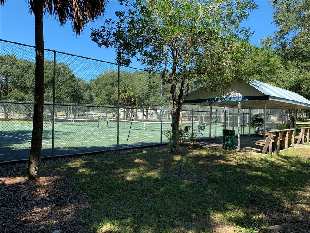 A fenced tennis court sits next to a covered seating area with wooden benches — 3550 N LAKESIDE VILLAGE DRIVE, BEVERLY HILLS, FL