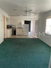 A living room with green carpeting leads to a kitchen with white cabinets and appliances — 804 WASHINGTON PALM LOOP UNIT 5, DAVENPORT, FL