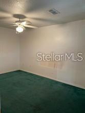 An empty room features green carpeting, white walls, and a ceiling fan with a light — 804 WASHINGTON PALM LOOP UNIT 5, DAVENPORT, FL