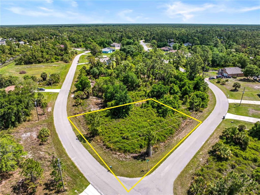 An aerial view shows a vacant, wooded corner lot outlined in yellow between two roads — 0 BARCELONA DRIVE Lot 1, NORTH PORT, FL
