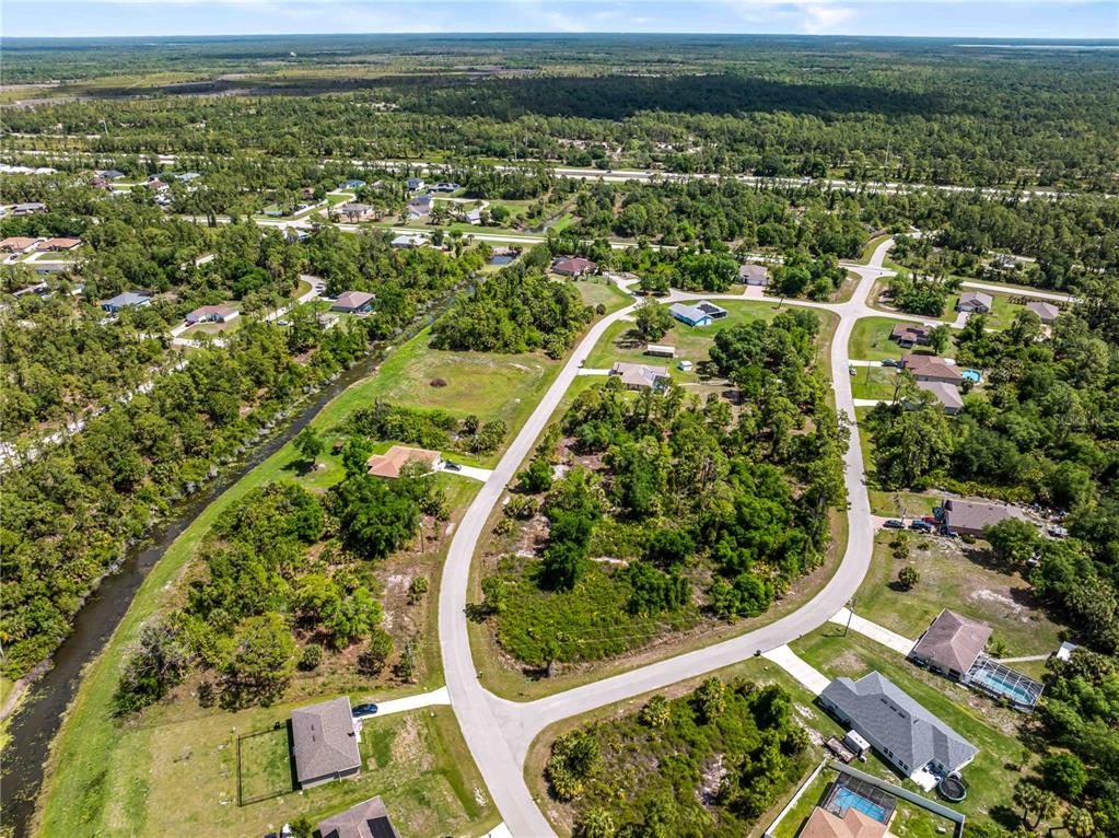 Aerial view of a suburban neighborhood with houses, wooded lots, and a winding canal — 0 BARCELONA DRIVE Lot 1, NORTH PORT, FL