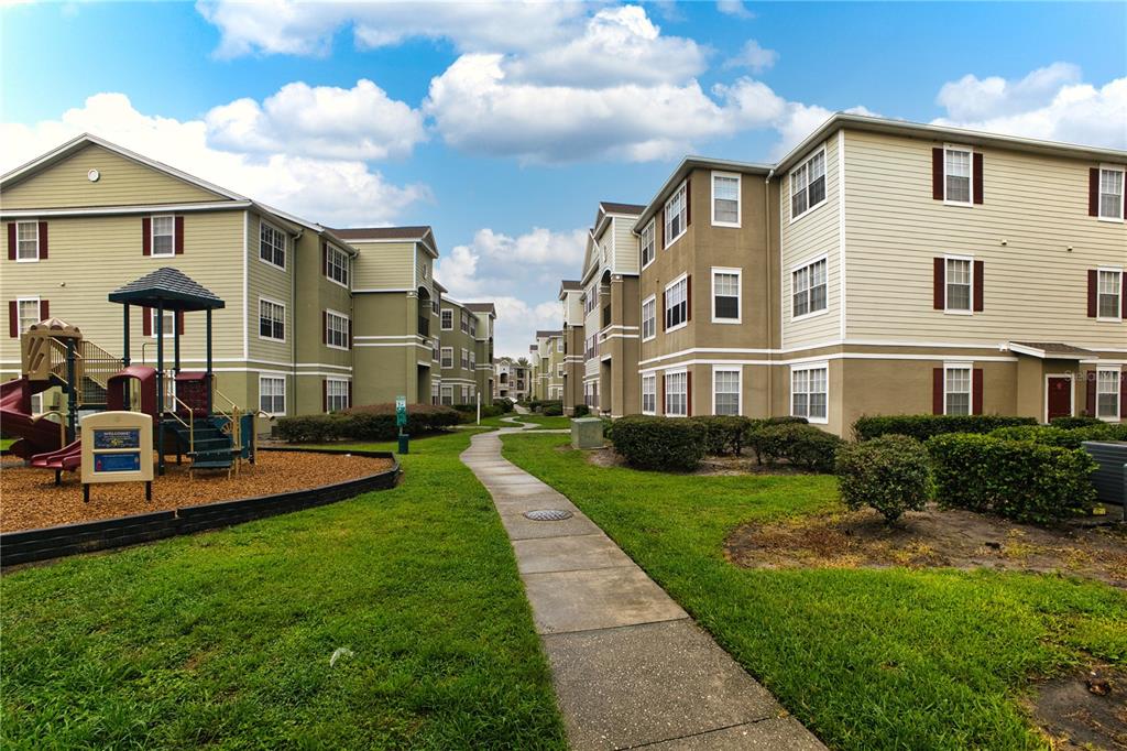 Exterior view of apartment buildings with a playground and a concrete walkway — 8225 CLAIRE ANN DR UNIT 203, ORLANDO, FL