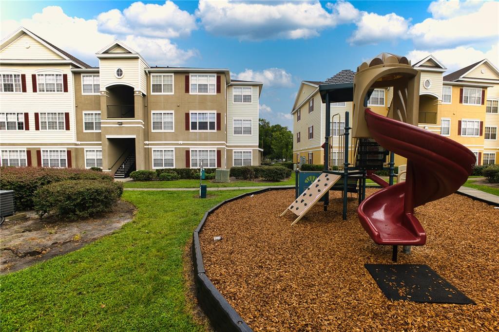 A playground with a red spiral slide sits in front of two multi-story apartment buildings — 8225 CLAIRE ANN DR UNIT 203, ORLANDO, FL
