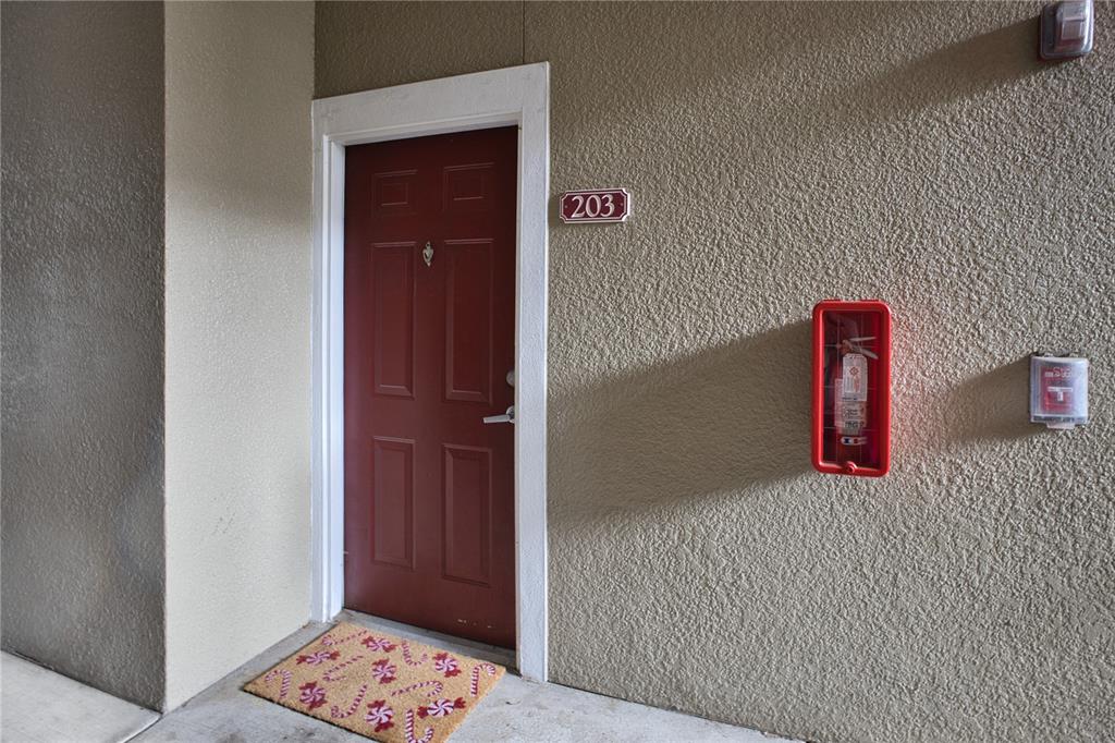 A red apartment door labeled 203 with a fire extinguisher mounted on the exterior wall — 8225 CLAIRE ANN DR UNIT 203, ORLANDO, FL
