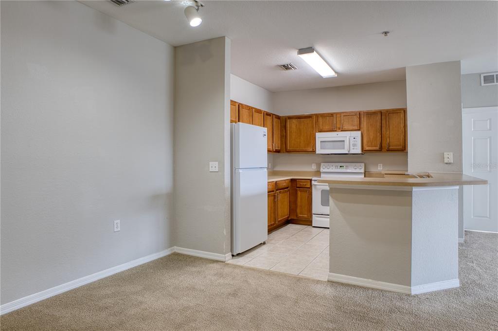 A kitchen with wood cabinets, white appliances, and a breakfast bar opens to a carpeted area — 8225 CLAIRE ANN DR UNIT 203, ORLANDO, FL