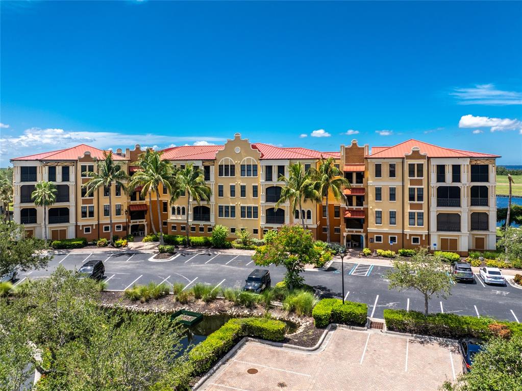 A multi-story yellow apartment building with a red roof sits behind a parking lot — 97 VIVANTE BOULEVARD UNIT 204, PUNTA GORDA, FL