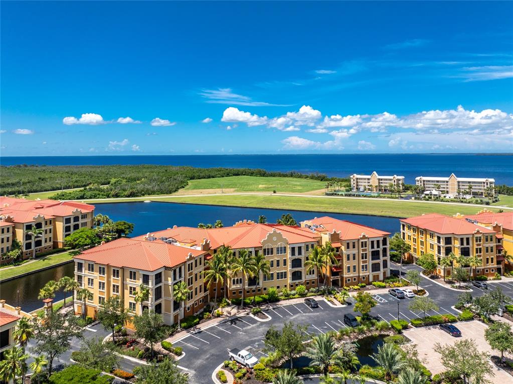 An aerial view shows multi-story apartment buildings with orange tile roofs near a lake — 97 VIVANTE BOULEVARD UNIT 204, PUNTA GORDA, FL