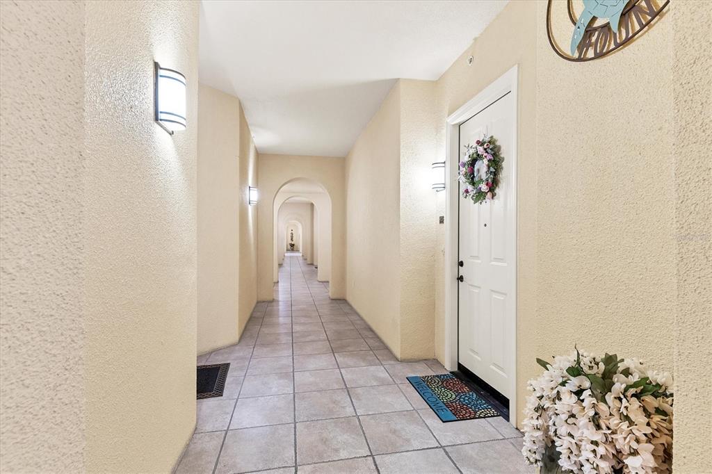 A long, tiled hallway features arched openings, wall sconces, and a white door with a wreath — 97 VIVANTE BOULEVARD UNIT 204, PUNTA GORDA, FL