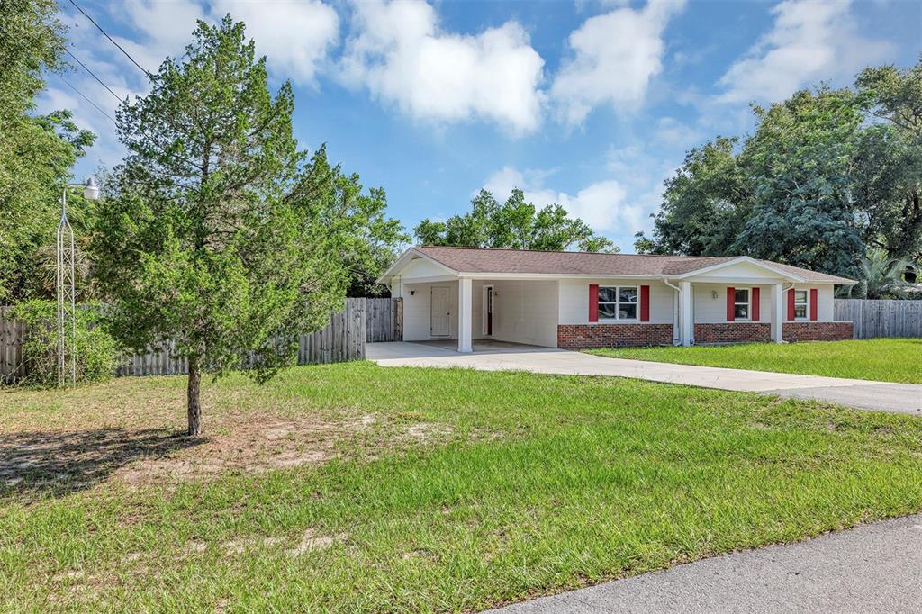 A single-story house with a carport, brick accents, and red shutters sits on a lawn — 9375 SE 163RD LANE, SUMMERFIELD, FL