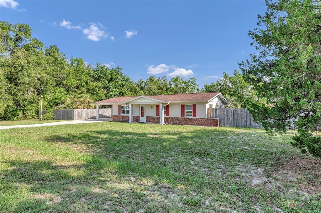 A single-story house with a brick base, light siding, and a carport sits on a lawn — 9375 SE 163RD LANE, SUMMERFIELD, FL