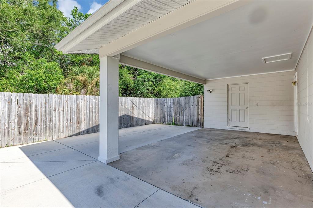A concrete carport with a white support pillar and a door leading into the home — 9375 SE 163RD LANE, SUMMERFIELD, FL