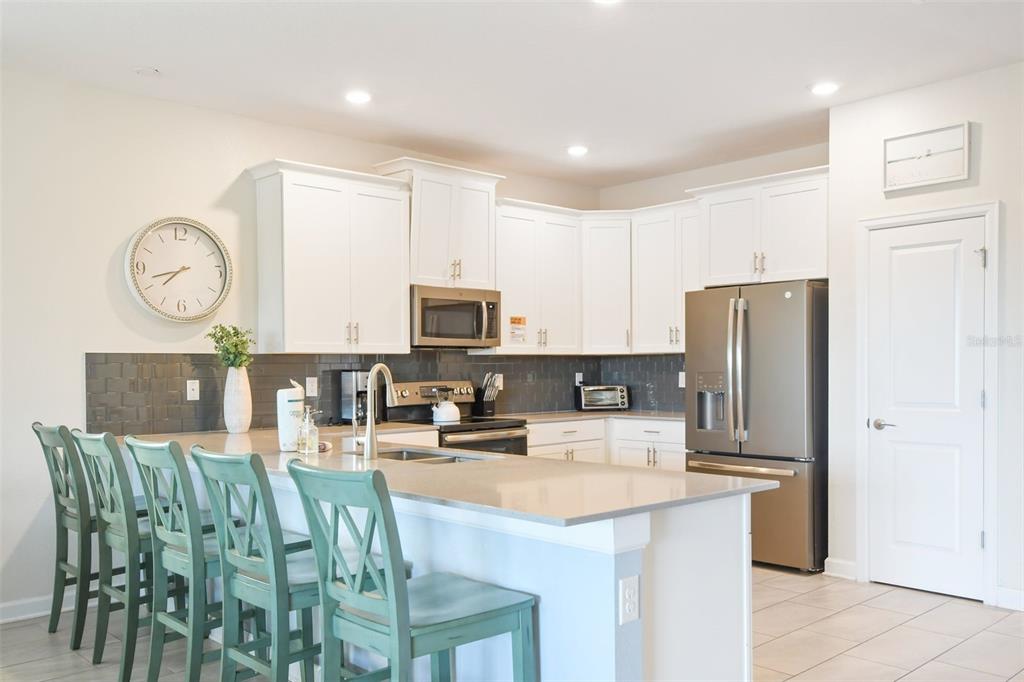 A kitchen features white cabinets, a gray tile backsplash, a kitchen island, and teal chairs — 2874 STANZA CT, KISSIMMEE, FL