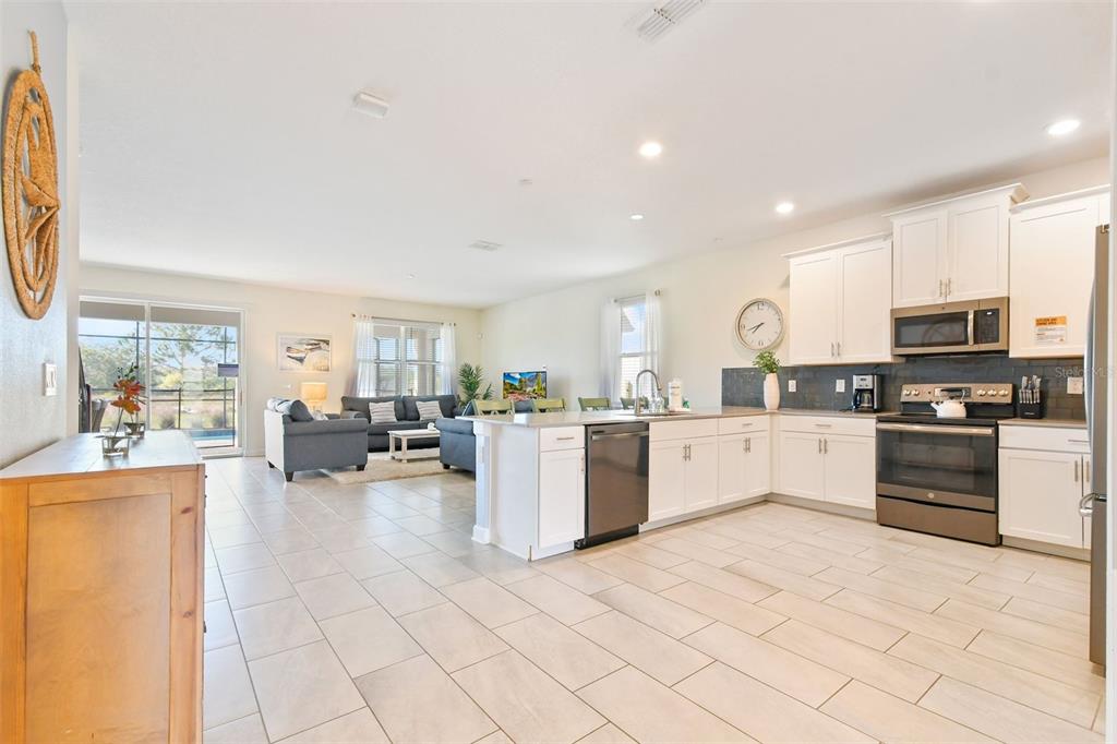 An open-concept kitchen with white cabinets and stainless steel appliances overlooks a living room area — 2874 STANZA CT, KISSIMMEE, FL