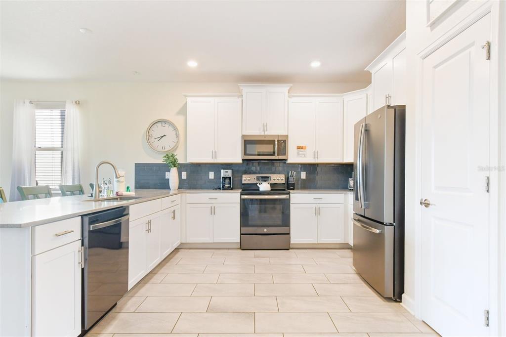 A kitchen features white cabinetry, stainless steel appliances, a dark tile backsplash, and tile flooring — 2874 STANZA CT, KISSIMMEE, FL