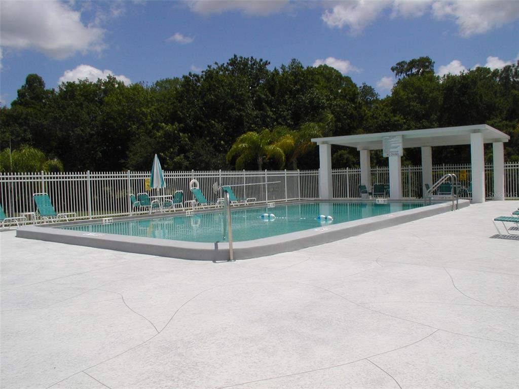 A rectangular outdoor swimming pool with a white fence and a covered patio area — 3952 ELVIRA COURT, NEW PORT RICHEY, FL