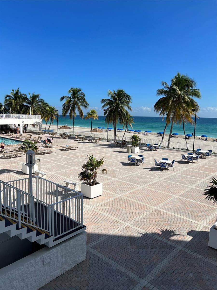 A paved outdoor patio features tables, chairs, and palm trees overlooking a beach and ocean — 2301 S Ocean Dr # 506, Hollywood FL 33019, HOLLYWOOD, FL