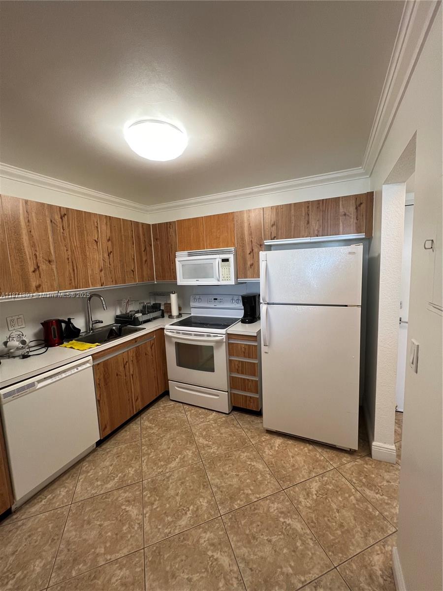 A kitchen features wood-grain cabinets, white appliances, and light-colored tile flooring — 2301 S Ocean Dr # 506, Hollywood FL 33019, HOLLYWOOD, FL