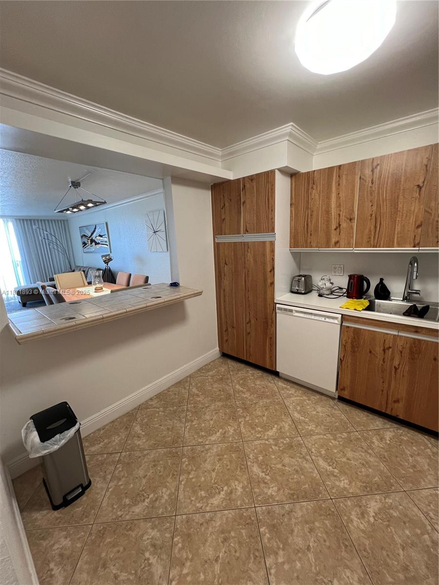 A kitchen features wood-grain cabinets, a tiled breakfast bar, and a view into the living area — 2301 S Ocean Dr # 506, Hollywood FL 33019, HOLLYWOOD, FL