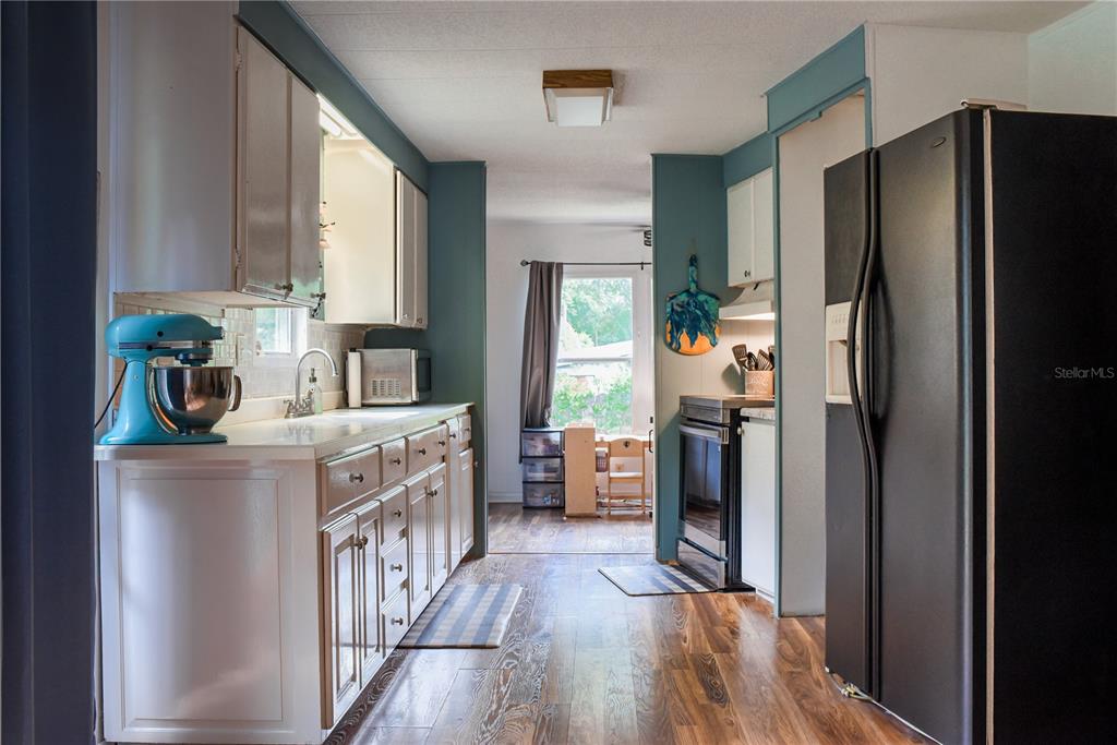 A kitchen features white cabinets, teal walls, a black refrigerator, and wood-look flooring — 5843 NE 167TH AVENUE, SILVER SPRINGS, FL