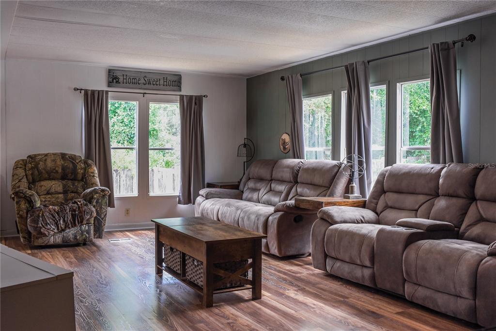 A living room features wood-look flooring, a camouflage recliner, and two brown reclining sofas — 5843 NE 167TH AVENUE, SILVER SPRINGS, FL