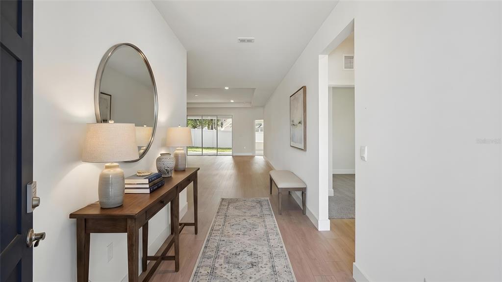 A bright entryway features a wooden console table, a round mirror, and light wood flooring — 17100 NW 180TH TERRACE, ALACHUA, FL