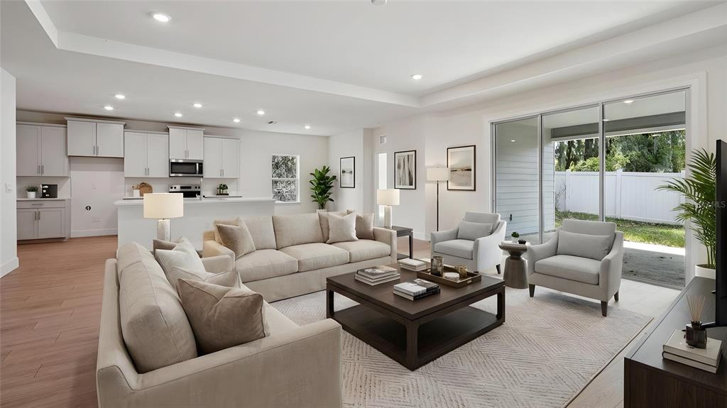 A bright open-concept living room features a kitchen, neutral furniture, and large sliding glass doors — 17100 NW 180TH TERRACE, ALACHUA, FL