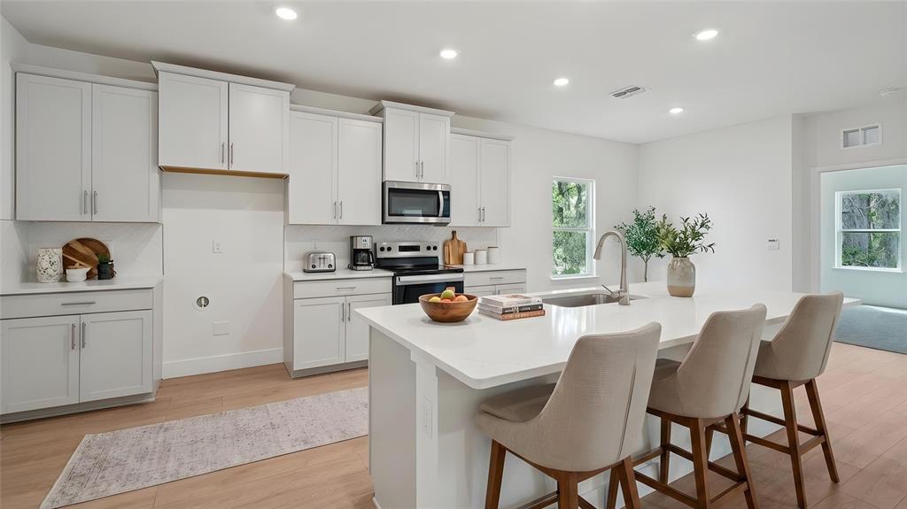 A modern kitchen features white cabinetry, a central island with bar seating, and light flooring — 17100 NW 180TH TERRACE, ALACHUA, FL