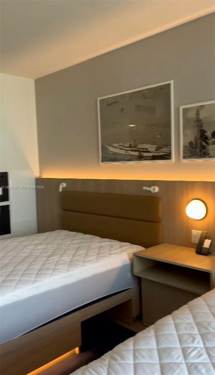 A bedroom features two beds, a wooden headboard with integrated lighting, and framed wall art — 159 NE 6th St # 1804, Miami FL 33132, MIAMI, FL