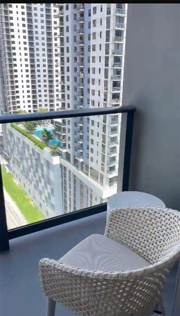 A balcony with a woven chair overlooks a tall apartment building and a swimming pool — 159 NE 6th St # 1804, Miami FL 33132, MIAMI, FL