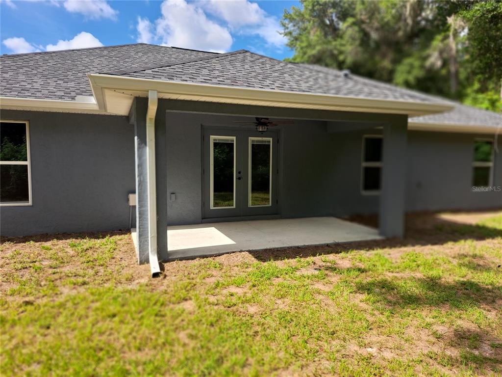 A gray stucco house exterior features a covered concrete patio with double glass doors — 547 GRAPEWOOD LN., CITRUS SPRINGS, FL