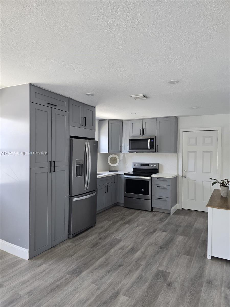 A kitchen features gray shaker-style cabinets, stainless steel appliances, and wood-look flooring — 719 21st St, West Palm Beach FL 33407, WEST PALM BEACH, FL