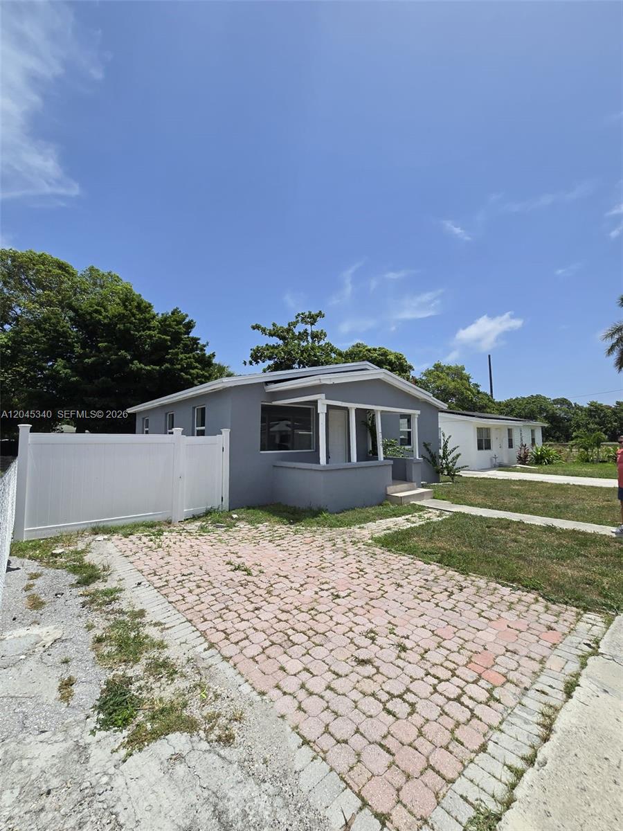 A gray single-story house features a paved driveway and a white vinyl privacy fence — 719 21st St, West Palm Beach FL 33407, WEST PALM BEACH, FL