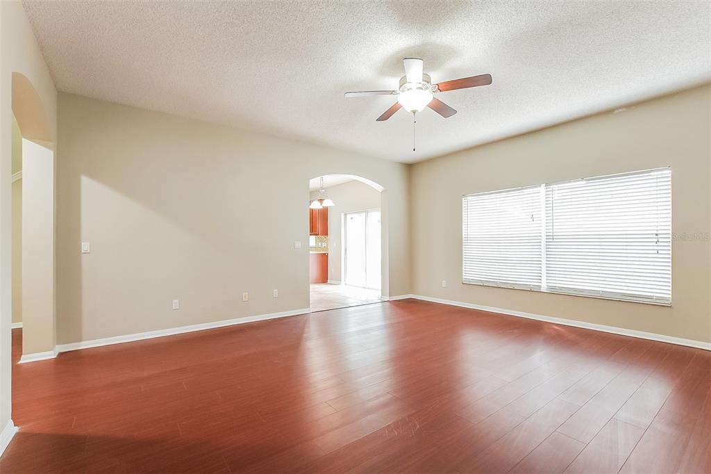 An empty living room features wood-look flooring, beige walls, a ceiling fan, and large windows — 2043 HAMMOCK MOSS DRIVE, ORLANDO, FL