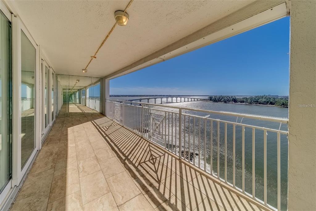 A long, tiled balcony features a white metal railing overlooking a bridge and water — 675 S GULFVIEW BOULEVARD UNIT PH1, CLEARWATER BEACH, FL