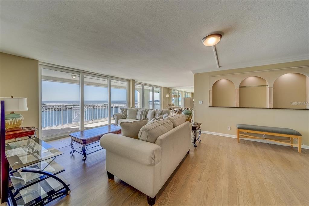 A living room features light wood flooring, a beige sofa, and large sliding glass balcony doors — 675 S GULFVIEW BOULEVARD UNIT PH1, CLEARWATER BEACH, FL