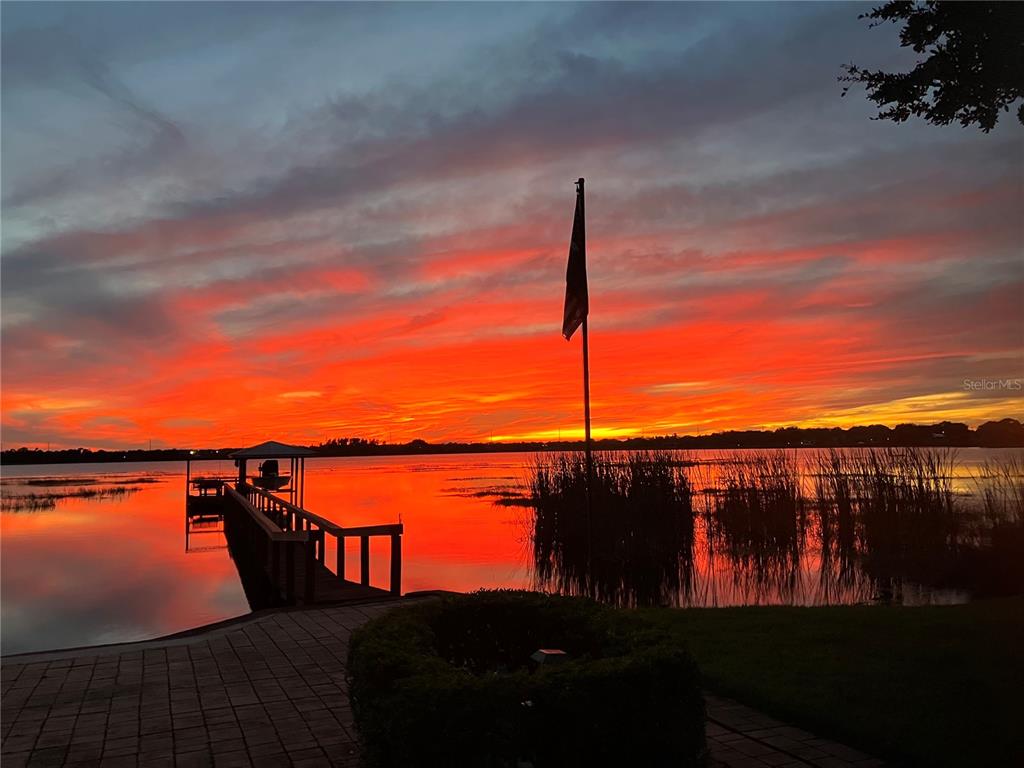 A vibrant sunset illuminates a lake with a wooden dock and a flag pole — 77 W LAKE DAMON DRIVE, AVON PARK, FL