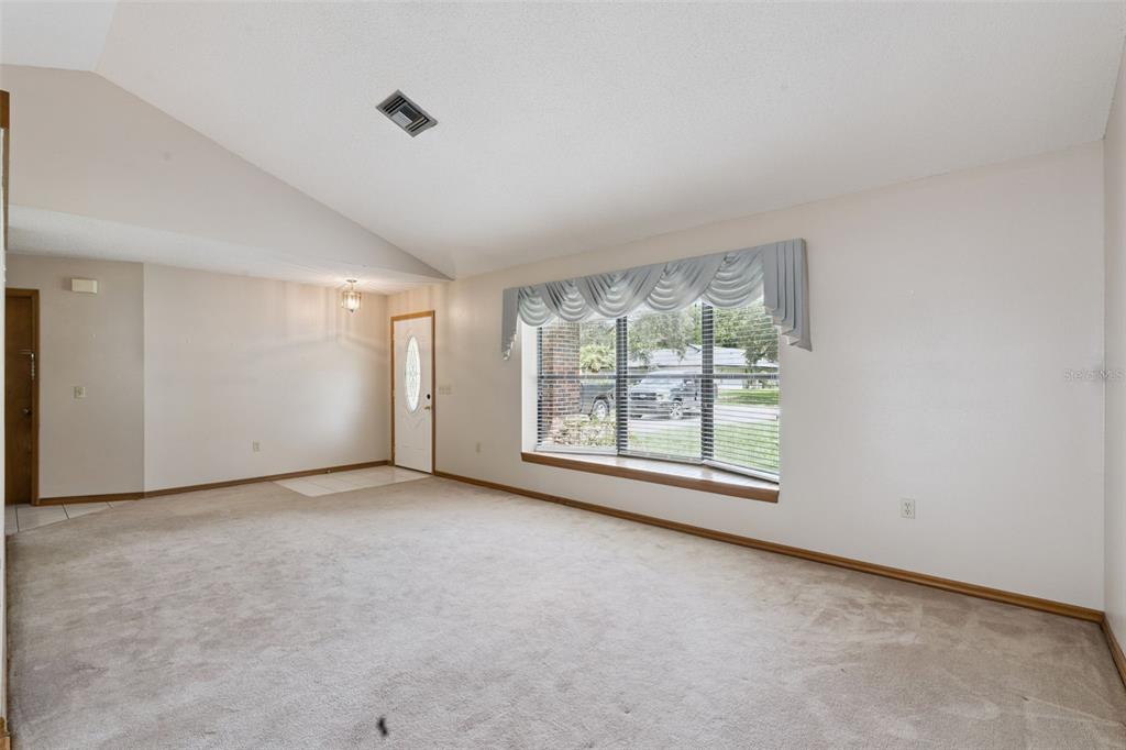 A living room with beige carpet, a vaulted ceiling, and a large bay window — 4160 WOOD DRIVE, MOUNT DORA, FL