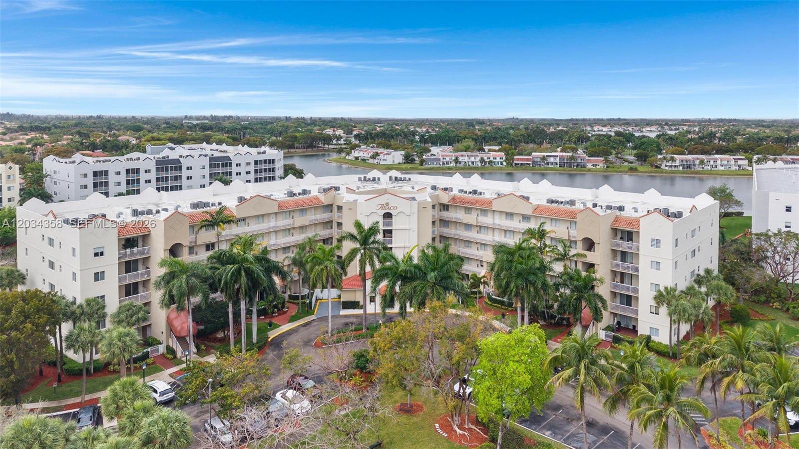 An aerial view shows a multi-story apartment complex with palm trees and a nearby lake — 10720 NW 66th St # 202, Doral FL 33178, DORAL, FL
