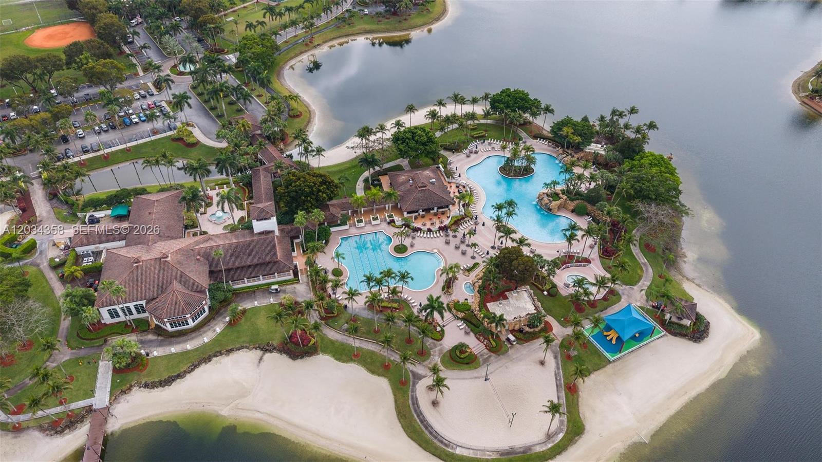 An aerial view shows a clubhouse, multiple swimming pools, and a sandy beach by a lake — 10720 NW 66th St # 202, Doral FL 33178, DORAL, FL