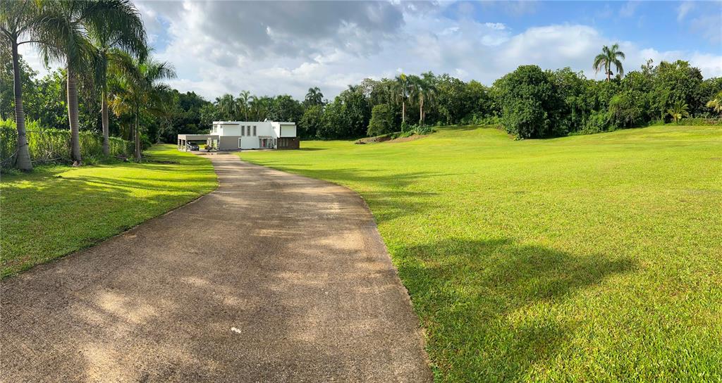 A paved driveway leads to a modern white house surrounded by a large grassy lawn — st.453 km5.5 BO PILETAS, LARES, PR
