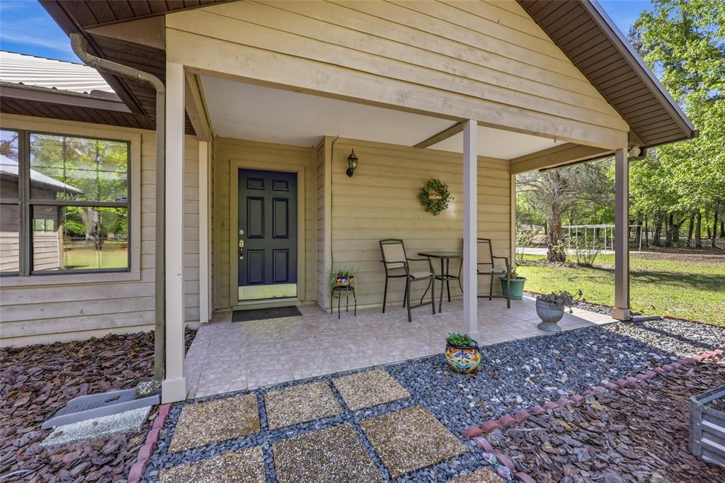 A covered front porch with a tiled floor, dark blue door, and outdoor seating area — 15223 NW STATE ROAD 45, HIGH SPRINGS, FL
