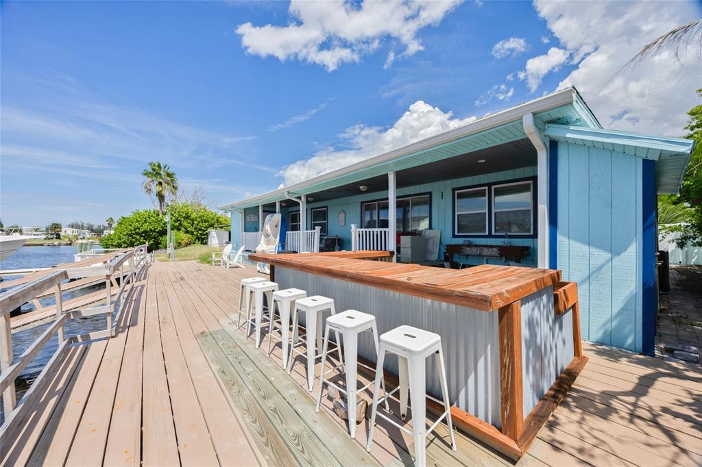 A light blue house features a wooden deck with a tiki bar and white stools — 13023 PORT COURT, HUDSON, FL