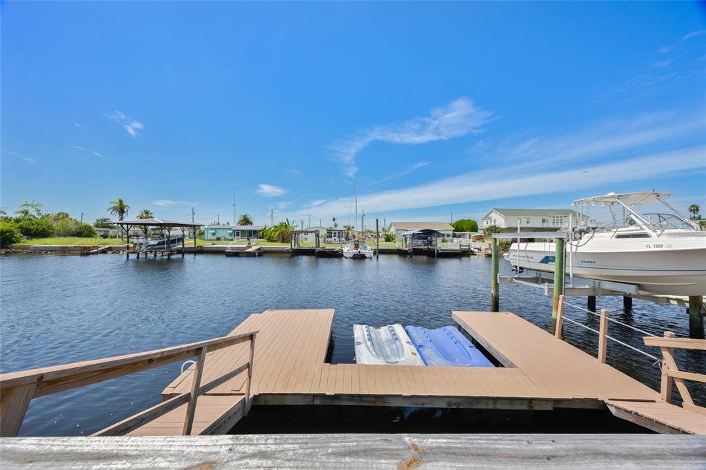 A wooden dock extends into a canal with boats and a boat lift nearby — 13023 PORT COURT, HUDSON, FL