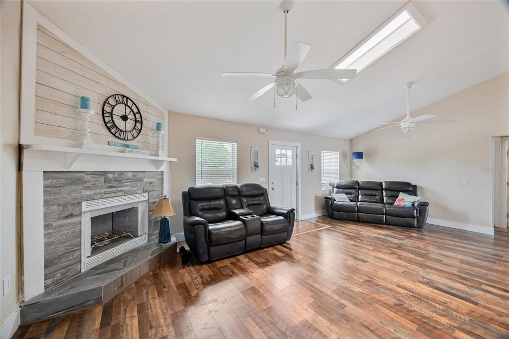 A living room features a stone fireplace, wood-look flooring, two leather sofas, and vaulted ceilings — 13023 PORT COURT, HUDSON, FL