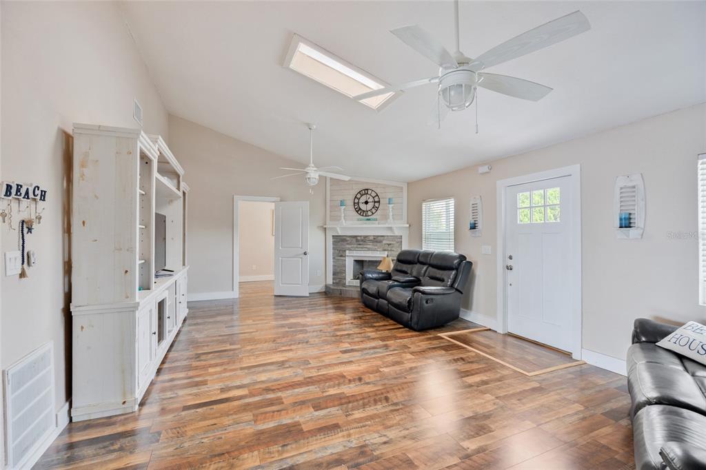 A living room with wood-look flooring, a stone fireplace, a ceiling fan, and white cabinetry — 13023 PORT COURT, HUDSON, FL