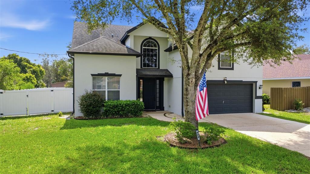 A two-story house with a white exterior, dark garage door, and a large front tree — 609 RHODES DRIVE, DELAND, FL